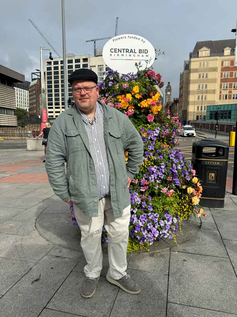 Person auf einem Vorplatz in Birmingham, im Hintergrund ein großer Blumenstrauß – ein Moment der Kreativpause.